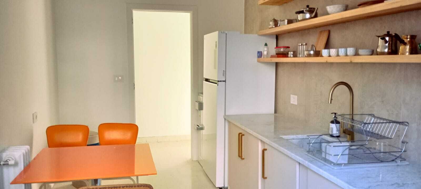 A compact kitchen with a dining table, chairs, a refrigerator, and a sink with a soap dispenser.