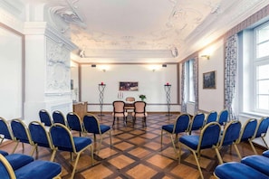 A conference room with a checkered floor, blue chairs, a table, and a painting on the wall.