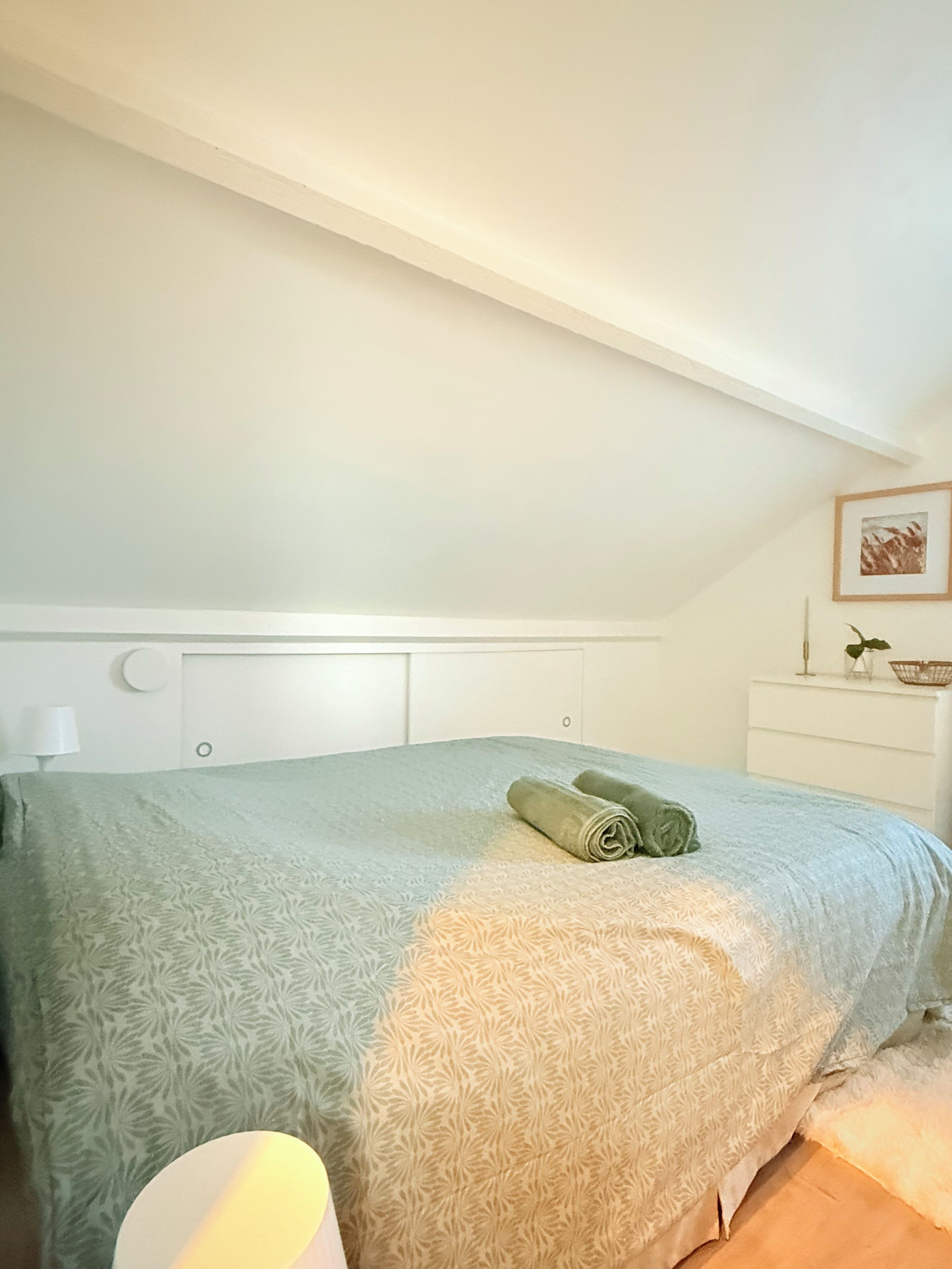 A bedroom with a bed, a bedside table, a lamp, and a framed picture on the wall.