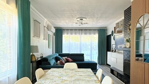 A dining area with a table set for four, a sofa, and a TV in the background. - Cosy House for 10 with clim and garden (Nivelles)