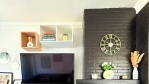 A living room with a flat-screen TV, white cabinetry, a black brick fireplace, and decorative items. - Cosy House for 10 with clim and garden (Nivelles)