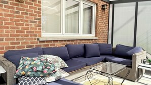 A covered outdoor seating area with a wicker sofa, a glass coffee table, and a patterned rug. - Cosy House for 10 with clim and garden (Nivelles)