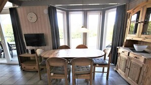 En matplats med ett runt träbord, fyra stolar, en klocka på väggen och en tv på ett stativ.