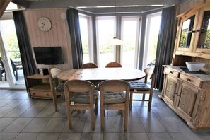 Ein Essbereich mit einem runden Holztisch, vier Stühlen, einer Wanduhr und einem Fernseher auf einem Schrank.