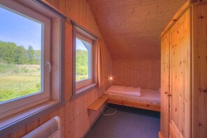 Ein kleines Zimmer in einer Holzhütte mit einem Einzelbett, einem Fenster und einer fest installierten Heizung.