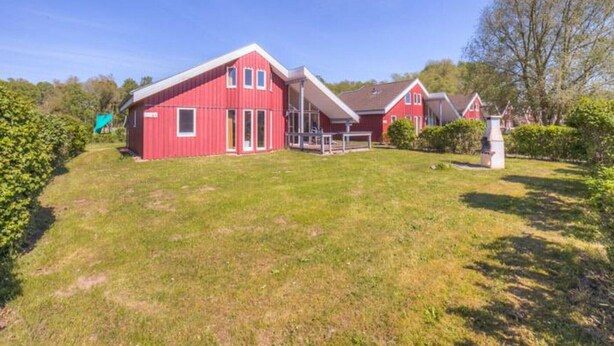 A red house with a sloped roof and a covered porch. - Ferienhaus im skandinavischen Stil mit Garten im Hafendorf Müritz (Rechlin)
