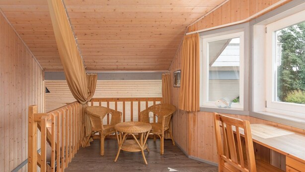 Una cabaña de madera con balcón, sillas de mimbre, una mesa de madera y un ventanal con vistas.