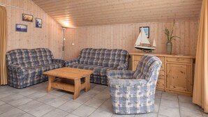 Una cabaña con paredes y techo de madera, dos sofás, una mesa de madera, un mueble pequeño y un modelo de velero.