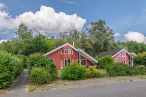 Eine Reihe roter Holzhäuser mit einem gepflasterten Weg, umgeben von Grünpflanzen und Bäumen.