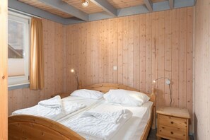 Habitación con paneles de madera, una cama, dos mesitas de noche y un ventanal con cortinas.