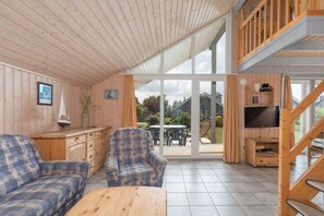 Ein gemütliches Interieur mit Holzwänden, einer Couch, einem Fernseher und Blick ins Freie.
