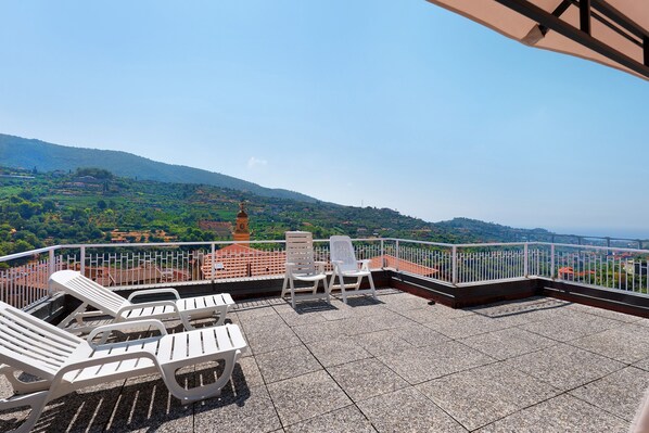 A terrace with white chairs and a table, overlooking a hilly landscape with a clock tower. - Apartment 'Rosetta' with Sea View, Wi-Fi and Air Conditioning (Vallebona)