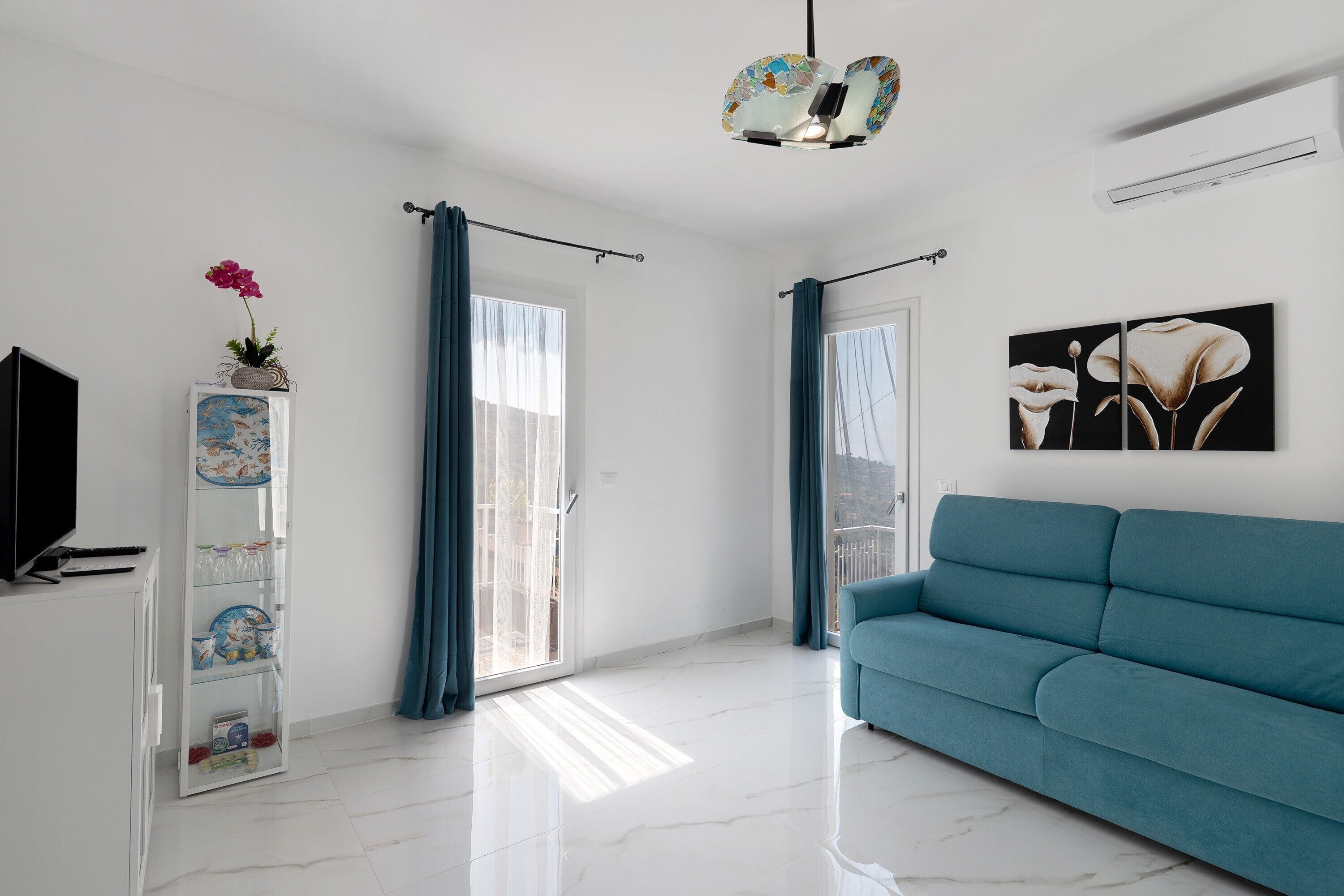 Uma sala de estar moderna com um sofá azul-turquesa, uma televisão, uma estante decorativa com uma planta e um quadro de flores.