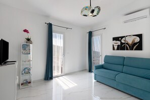 A modern living room with a teal sofa, a television, a decorative shelf with a plant, and a painting of flowers.