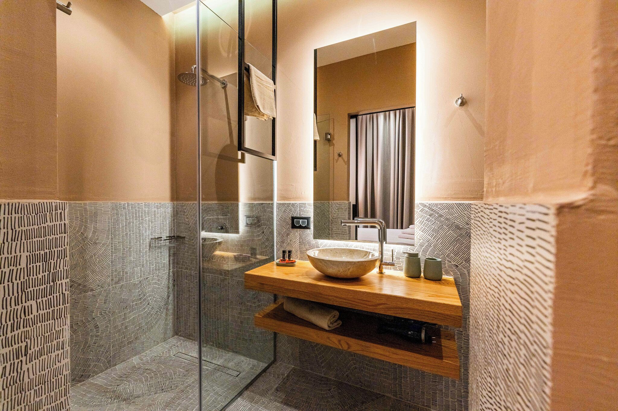 A modern bathroom with a glass shower enclosure, a wooden vanity with a bowl sink, and a mirror above the sink.
