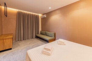 Una habitación de hotel con una cama, un pequeño sofá, una mesita de madera y un aire acondicionado instalado en la pared.