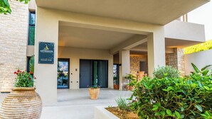 A modern building entrance with a sign for Aetherion Apartments, a boutique living area, and a well-maintained outdoor garden. - Aetherion Suites (Chania)