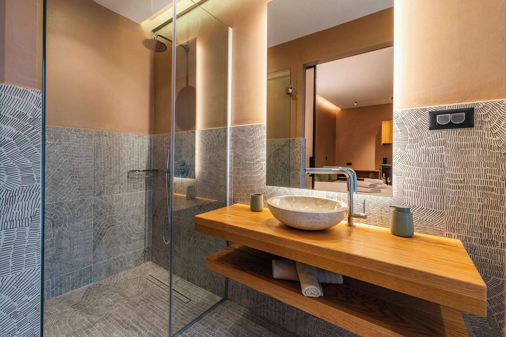 A modern bathroom with a glass shower enclosure, a wooden vanity with a bowl sink, and patterned walls.
