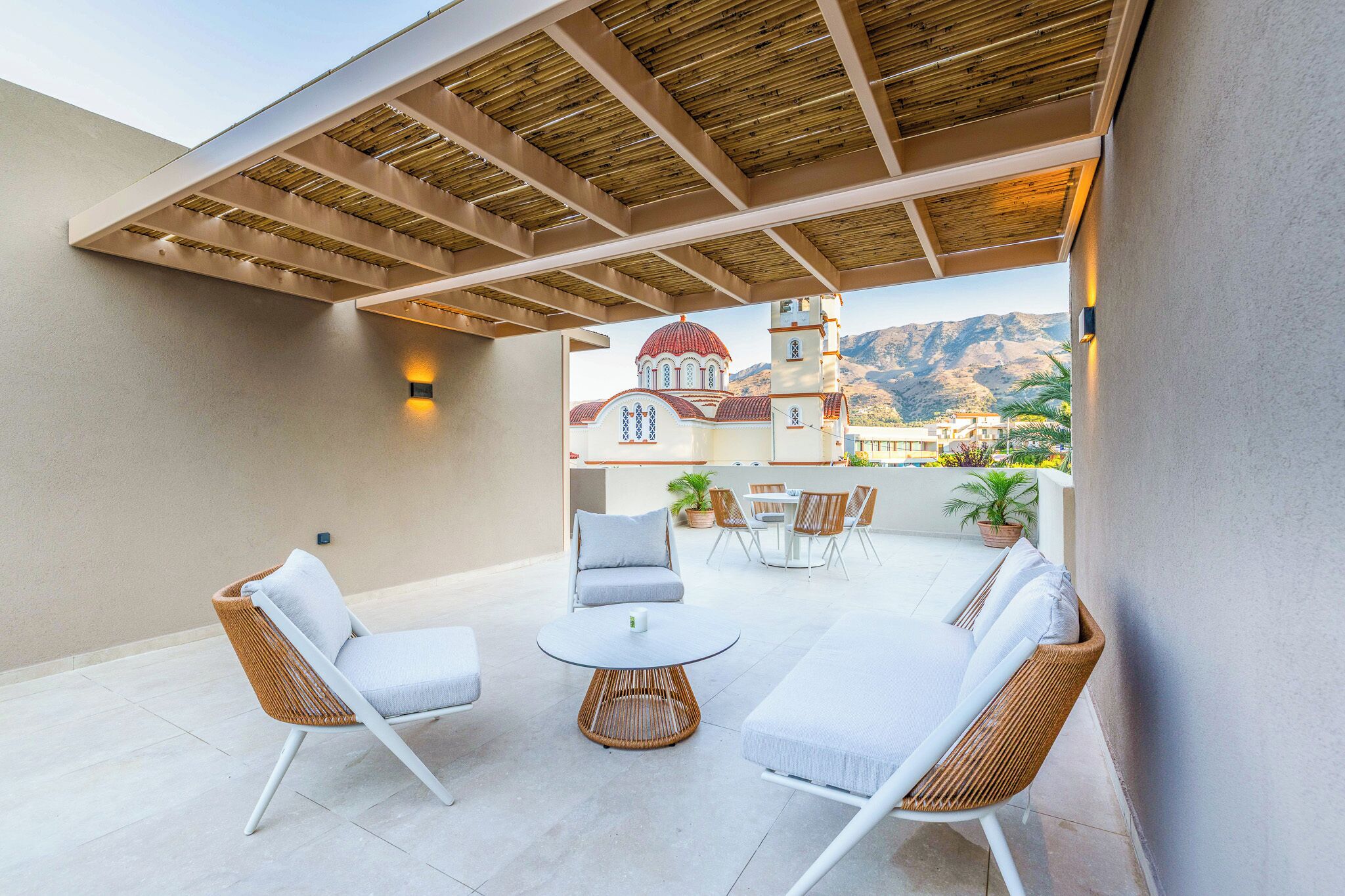 An outdoor patio with wicker furniture, a round table, and a view of a mountain and a building.