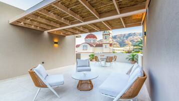 An outdoor patio with wicker furniture, a round table, and a view of a mountain and a building.