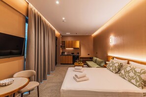 A hotel room with a bed, a TV, a desk, a chair, a sofa, and a kitchenette. - Aetherion Suites (Chania)
