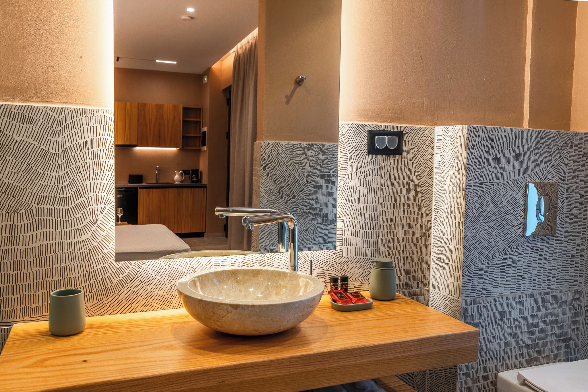 Een moderne badkamer met een grote wasbak, een houten aanrechtblad, betegelde muren met een patroon en een spiegel.