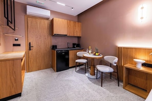 A compact kitchen with a dining area, including a table with chairs, a coffee machine, and a fruit bowl. - Aetherion Suites (Chania)