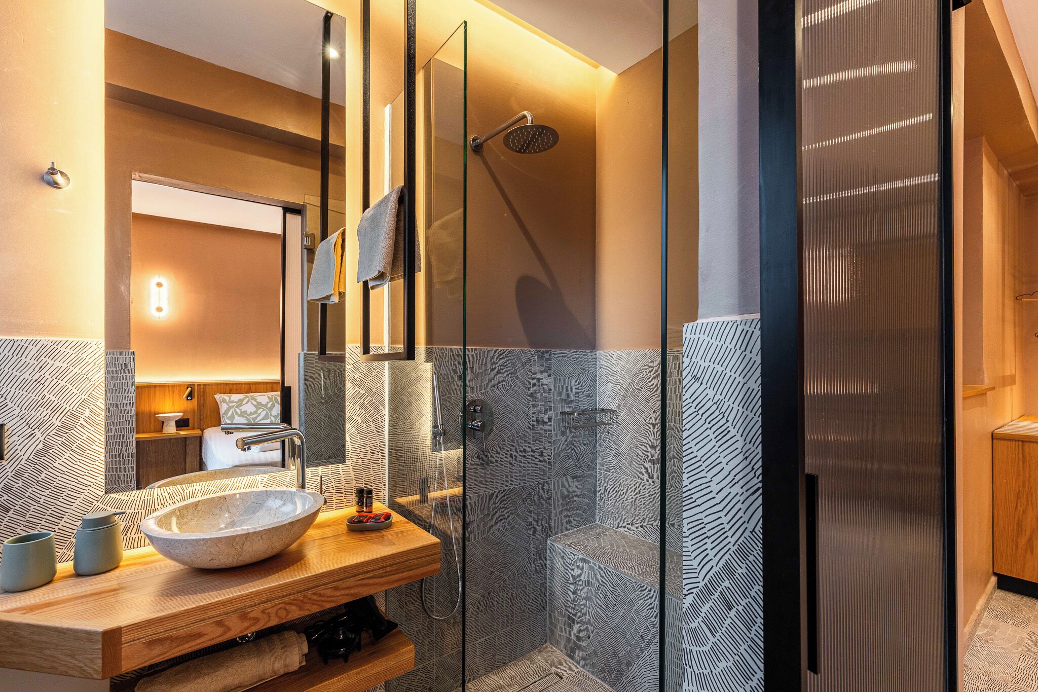 Un baño moderno con mampara de vidrio, tocador de madera con un lavabo grande y un espejo sobre el lavabo.