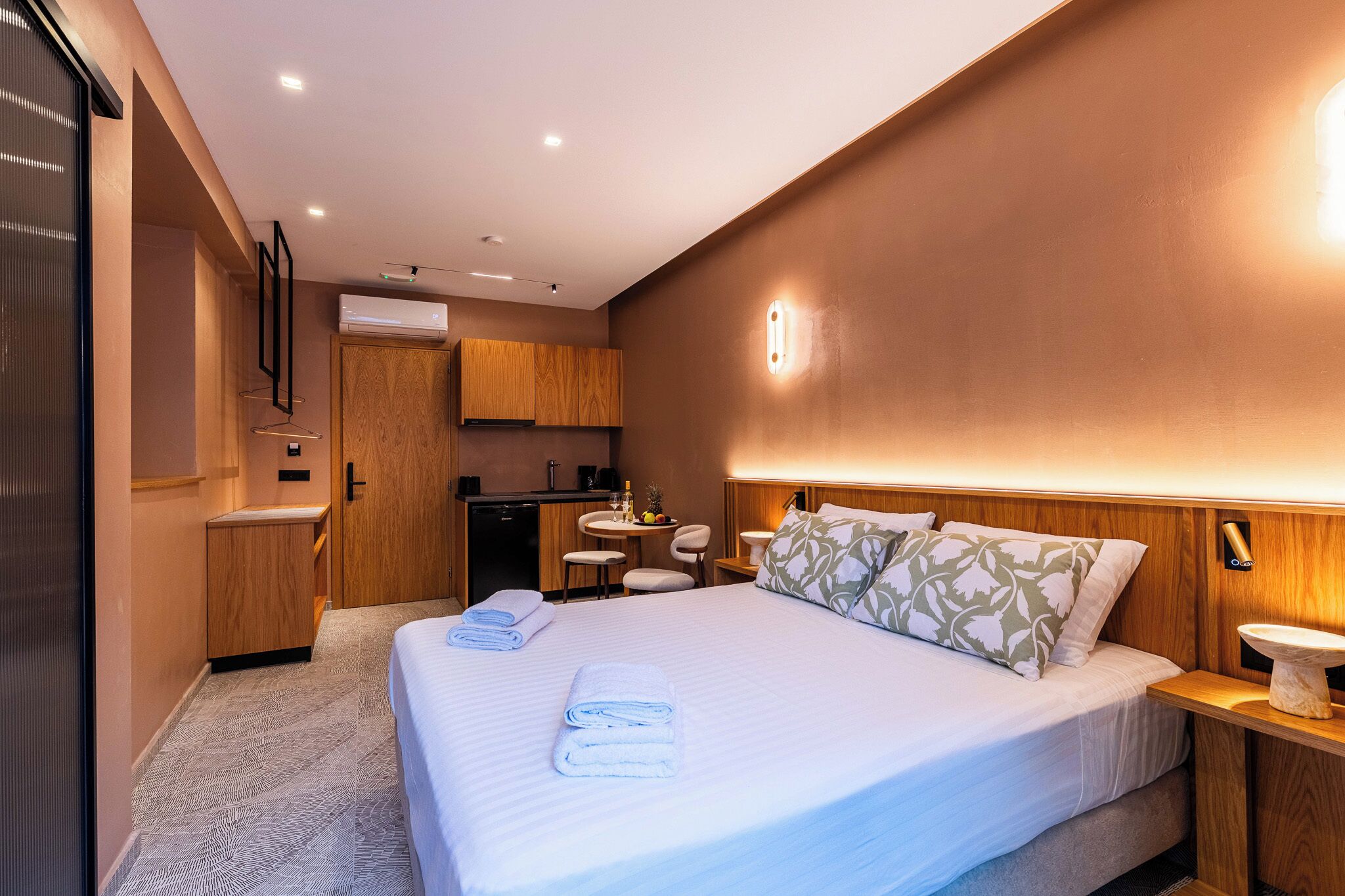 A hotel room with a bed, bedside tables, a small kitchenette, and a bathroom.