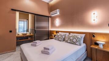 Habitación de hotel con cama, mesita de noche, espejo, ventana y aire acondicionado.