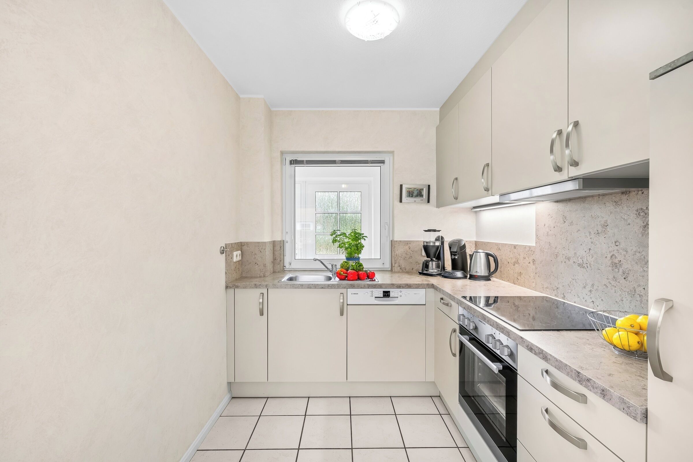 A compact kitchen with a window, stainless steel appliances, and a tiled floor.
