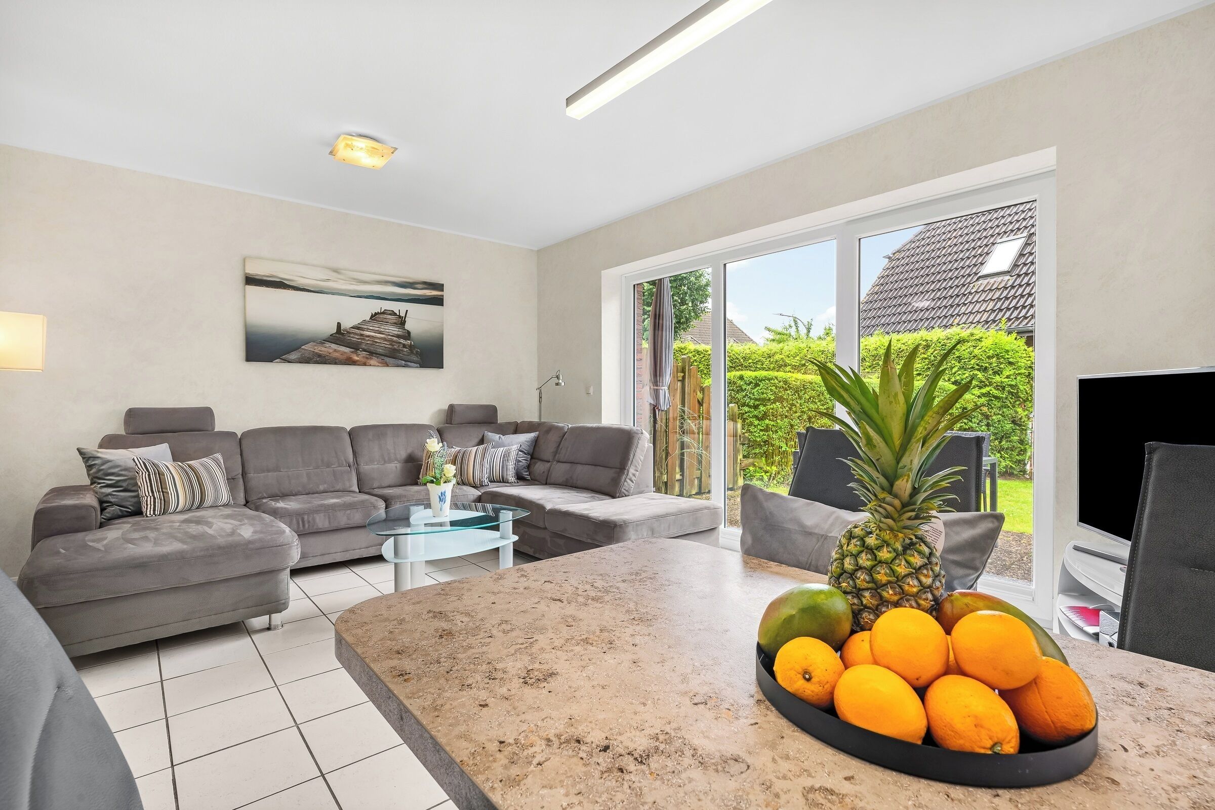 A modern living room with a grey sofa, a coffee table, and a fruit bowl on the kitchen island.