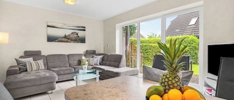 A modern living room with a grey sofa, a coffee table, and a fruit bowl on the kitchen island.