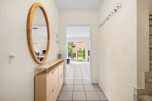 A hallway with a wooden cabinet, a large mirror, and a white door leading to an outdoor area. - Enjoy a relaxing getaway at the "Küstenzeit SPO" vacation apartment. (Sankt Peter-Ording)