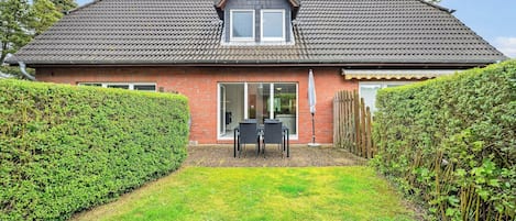Une maison à deux étages, avec un toit en tuiles, une porte d’entrée et un petit patio aménagé avec du mobilier d’extérieur.