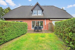 Ein zweigeschossiges Haus mit Ziegeldach, einer Haustür und einer kleinen Terrasse mit Gartenmöbeln.