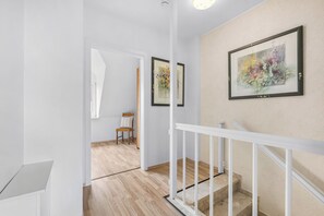 Una escala amb baranes blanques, un sostre de fusta i una obra d'art floral emmarcada a la paret.