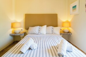 A hotel room with a striped bed, two bedside lamps, a headboard, and a framed picture on the wall. - SEAS THE DAY (Luz)