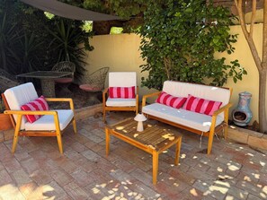 Ein Außenbereich mit einer Holzterrasse, zwei weißen Sofas mit roten Kissen und zwei Metallstühlen.