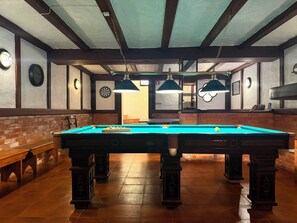 A pool table with a green felt surface, surrounded by wooden benches and tables. - SEAS THE DAY (Luz)