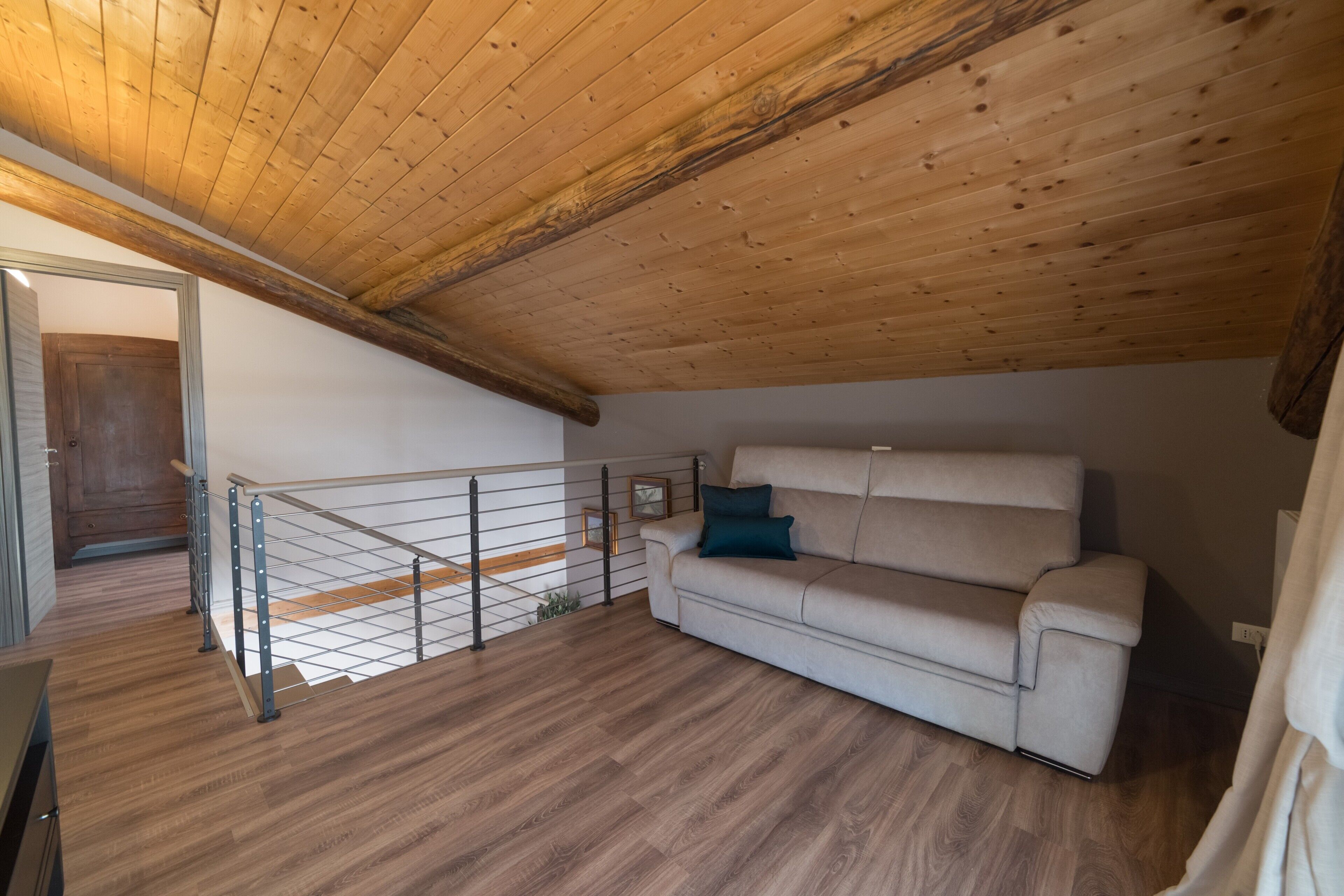 Un espai tipus loft amb sostre de fusta, un sofà, barana metàl·lica i terra de fusta.