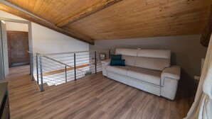 Een loftkamer met houten plafond, een bank, een metalen leuning en een houten vloer.