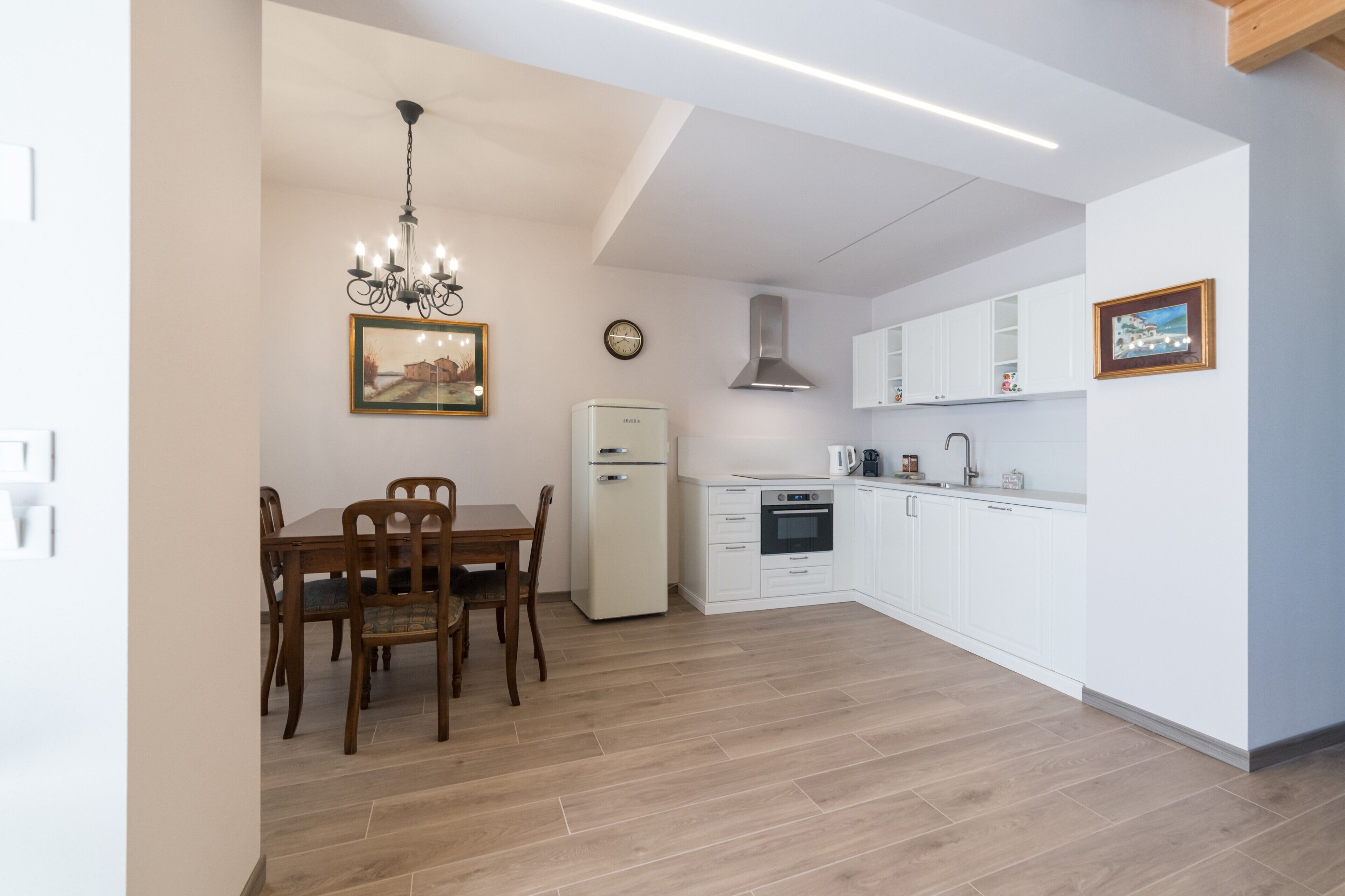 Una cucina moderna con mobili bianchi, forno integrato e zona pranzo con sedie di legno.