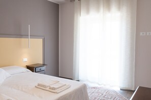 Et hotelværelse med seng, et natbord, en lampe og et vindue med gardiner.