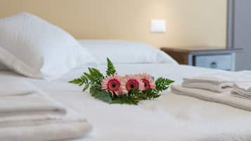 Un letto rifatto con lenzuola bianche, un piccolo bouquet di fiori e un comodino con una lampada.