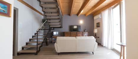 Una escalera conduce a una zona superior con un sofá blanco y un televisor de pantalla plana.