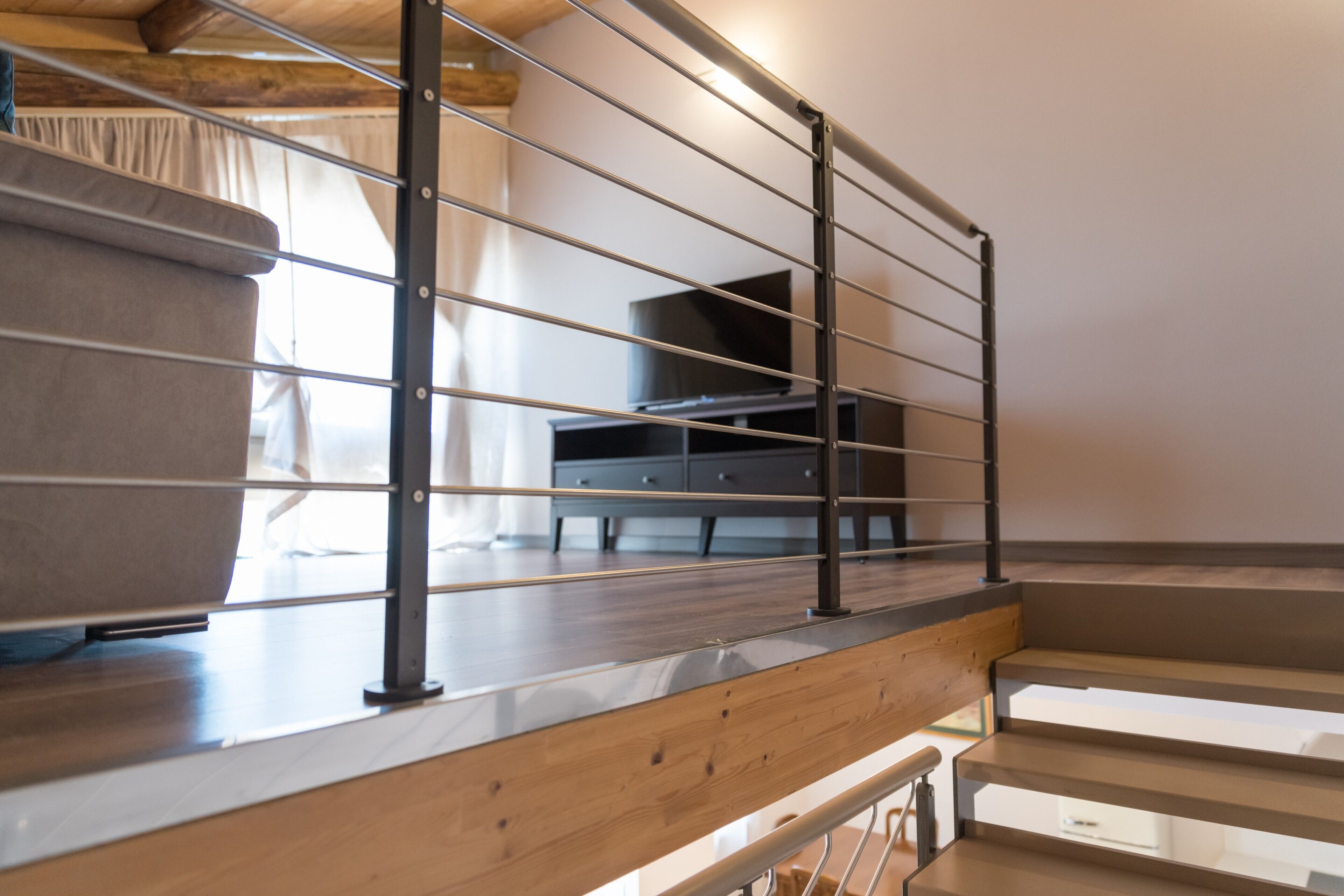 A wooden staircase with metal railings, a flat-screen TV, and a sofa in a modern interior.