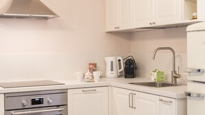Uma cozinha moderna com armários brancos, exaustor de aço inoxidável, forno embutido, cafeteira e pia.