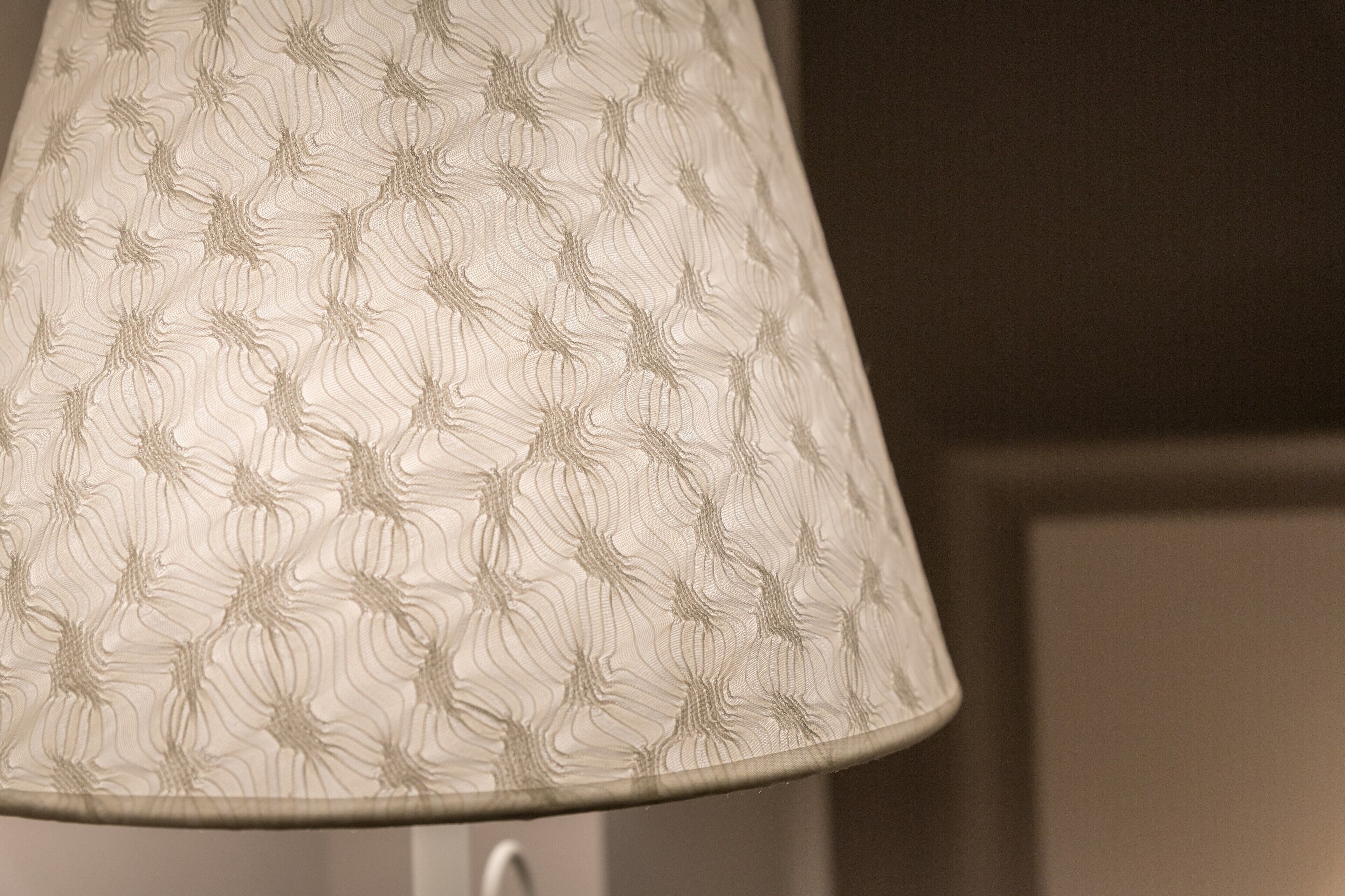 Tæt påsyn af en lampe med en skærm i stof med struktur.