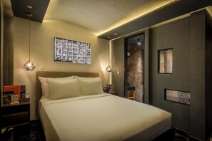 Habitación de hotel con una cama grande, una obra de arte en la pared, una mesita de noche y una puerta que da al baño.